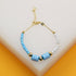 A dainty gold chain bracelet features alternating light blue and white seed beads accented by striped cylinder beads.