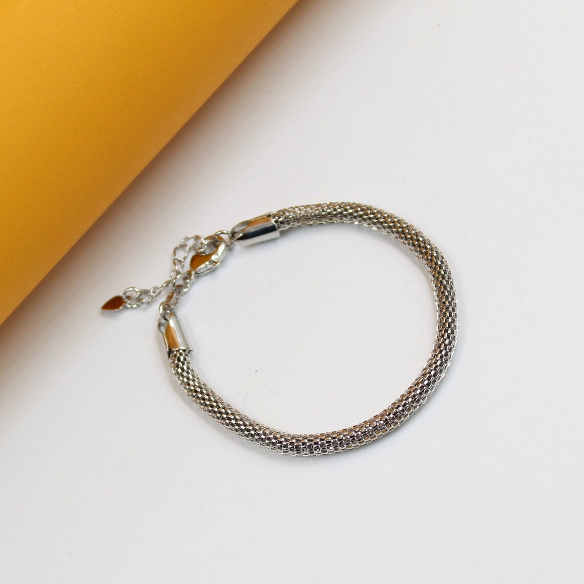 A silver mesh chain bracelet rests on a white and yellow surface.