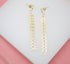 A pair of gold dangle earrings featuring long chains of textured chevron links rest on a white surface.
