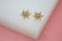 A pair of gold starburst stud earrings with central sparkling crystals rests on a white display block.