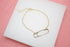 A delicate gold chain bracelet features a unique safety pin charm resting on a white display surface.