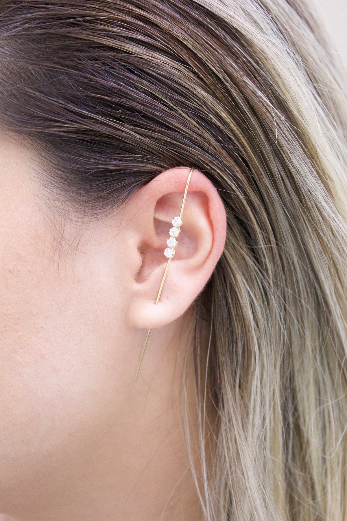 A close-up of a person wearing a delicate gold bar ear climber adorned with four sparkling diamonds.