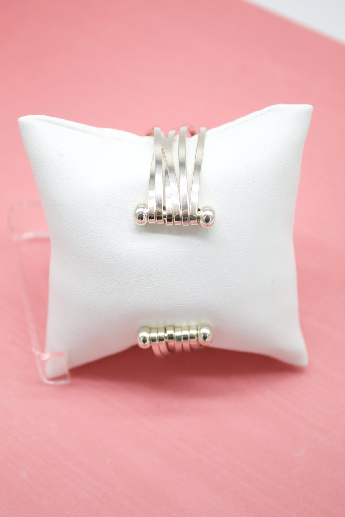 A unique sterling silver ring featuring multiple interconnected bands displays on a white velvet jewelry pillow against a pink background.