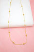 A delicate gold chain necklace with evenly spaced faceted bead stations rests on a white display surface against a pink background.