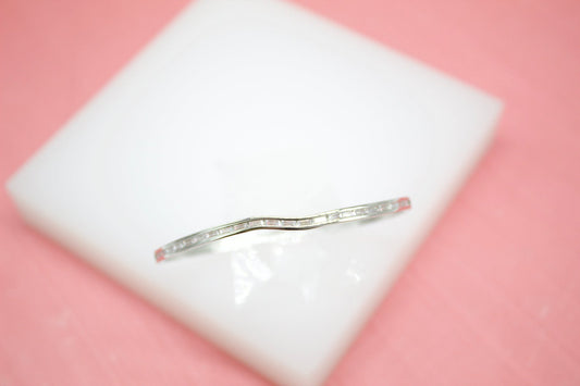 A curved silver diamond band rests on a white display square against a soft pink background.