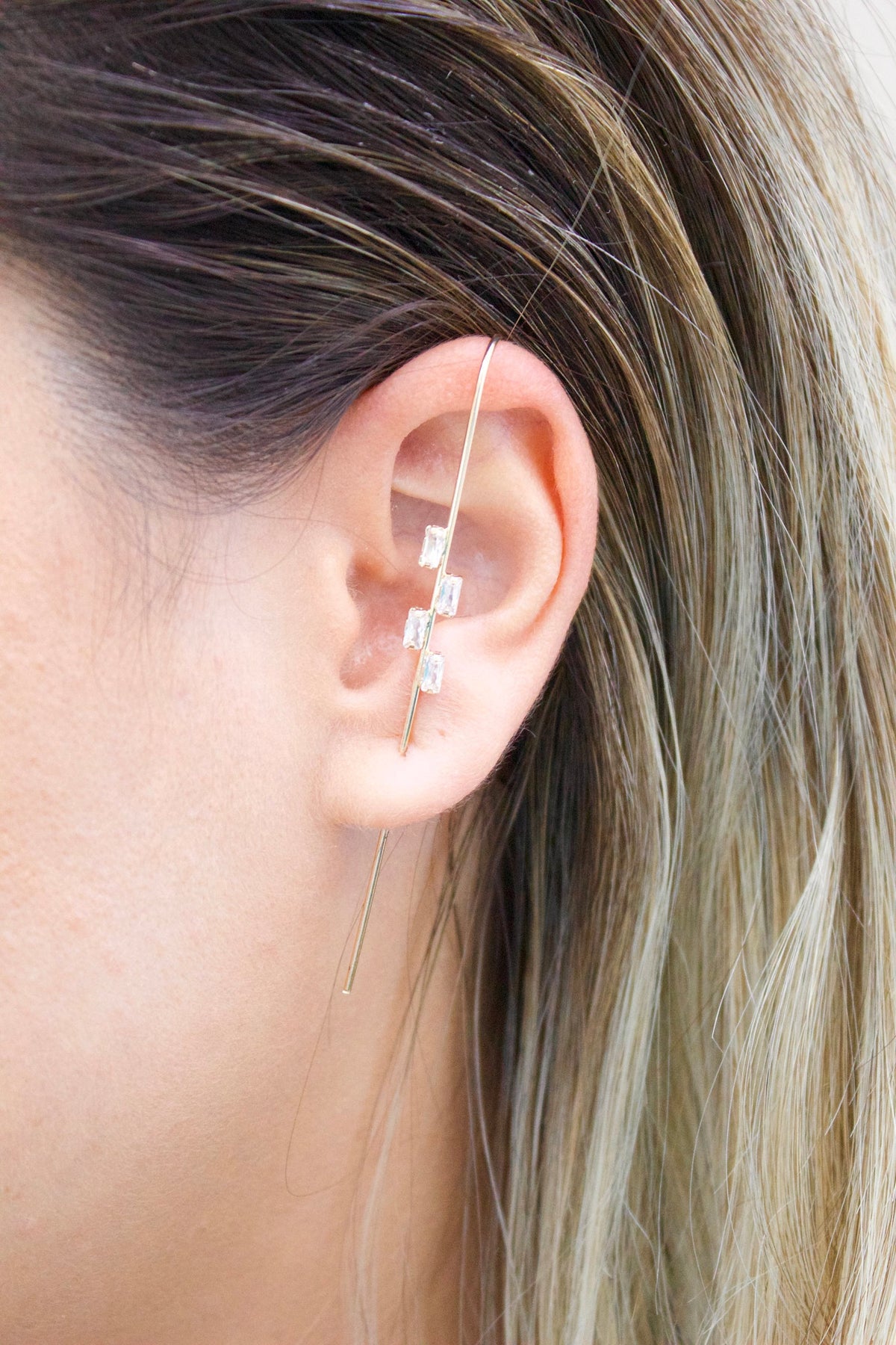 A woman wears a modern gold ear crawler with sparkling baguette-cut zirconia stones along her outer ear cartilage.