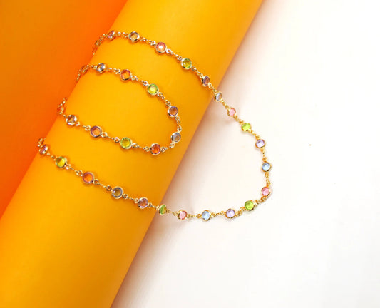 A delicate gold chain necklace sparkles with colorful gemstone stations draped gracefully across a vibrant orange and white background.