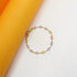 A dainty gold chain bracelet featuring multi-colored bezel-set crystals lies on a curved white and orange background.