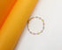 A delicate gold chain bracelet featuring colorful, bezel-set cubic zirconia stones rests against a vibrant yellow and white background.