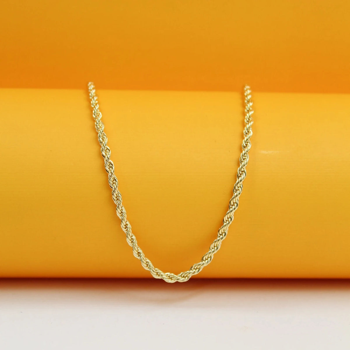 A gleaming gold rope chain necklace drapes elegantly over a bright yellow display cylinder.