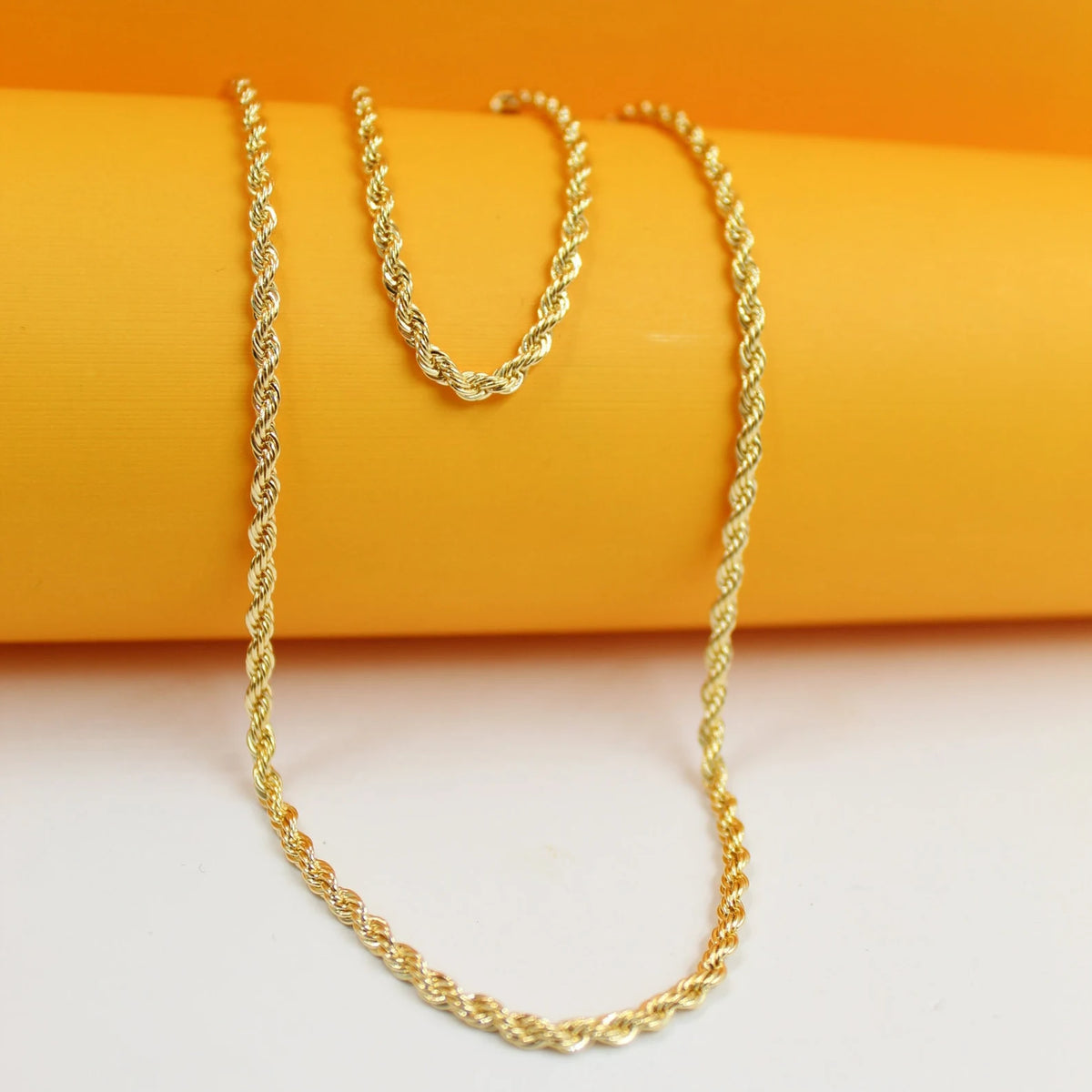 A gleaming gold rope chain necklace drapes gracefully against a vibrant orange and white backdrop.