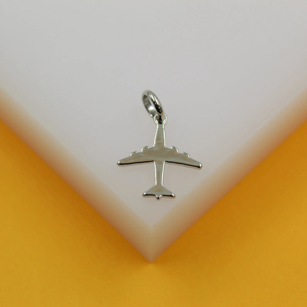 A silver airplane pendant rests on a white display block against an orange background.