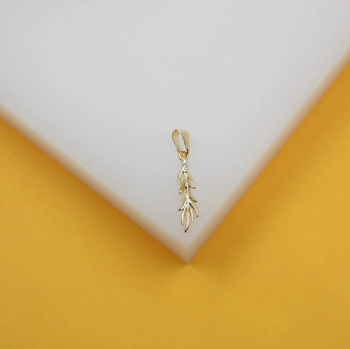 A delicate gold leaf pendant hangs on a white and yellow display block.