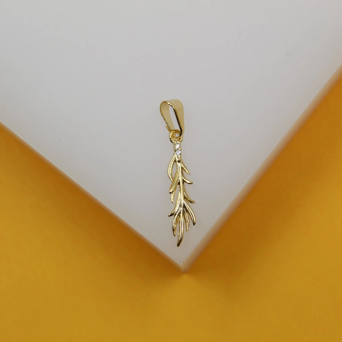A delicate gold leaf pendant sparkles with tiny cubic zirconia stones against a white and yellow backdrop.