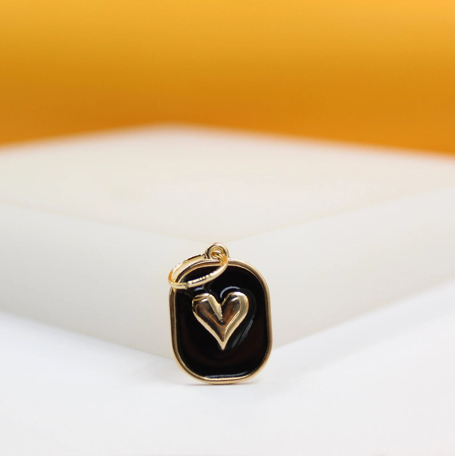 A gold-plated pendant features a raised golden heart set against a black enamel background inside a rounded rectangular frame.