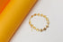 A delicate gold butterfly bracelet rests on a white surface next to a yellow cylinder.