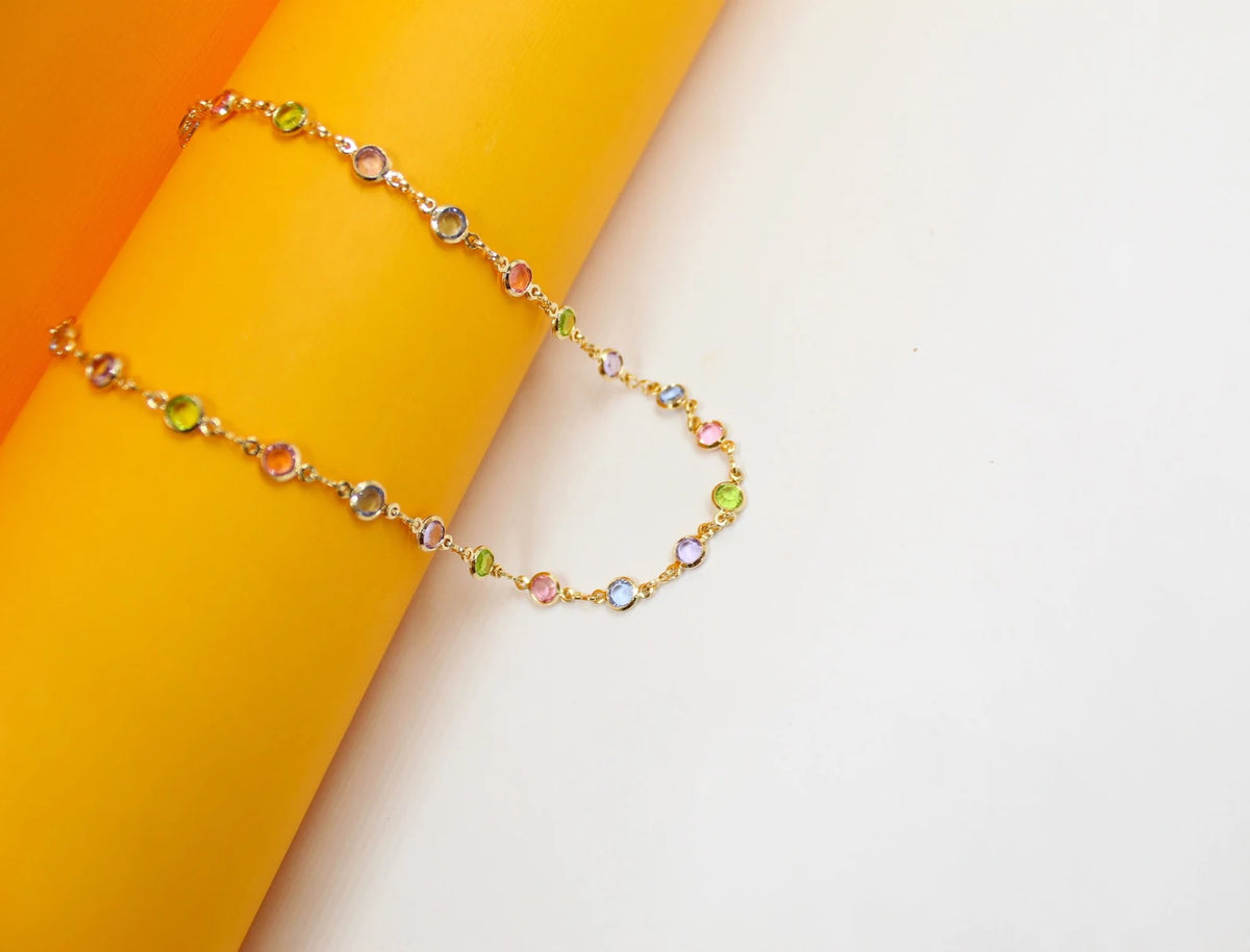A delicate gold multi-colored gemstone necklace drapes gracefully against a vibrant yellow and white background.