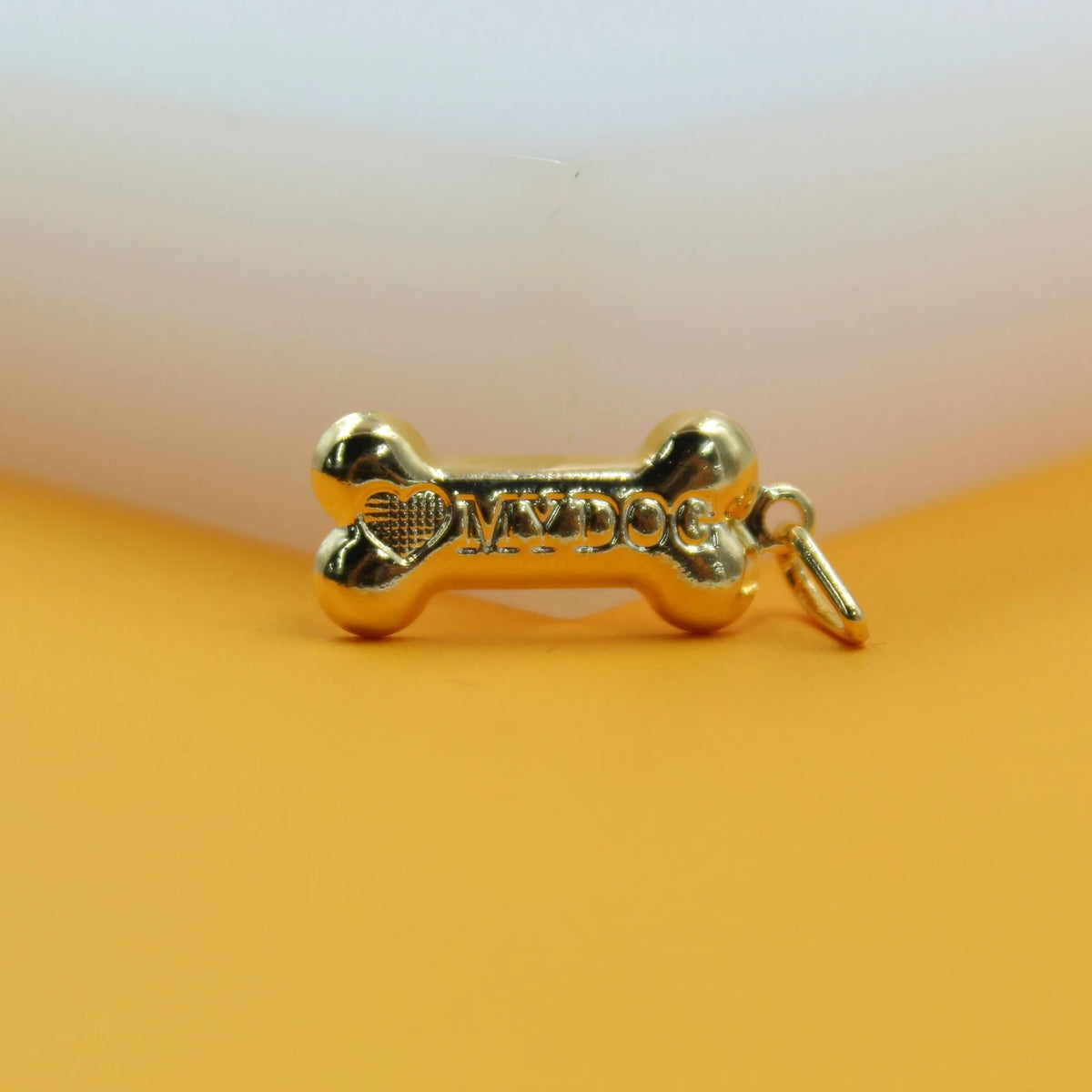 A polished gold bone pendant engraved with the words "I love my dog" rests on an orange surface.