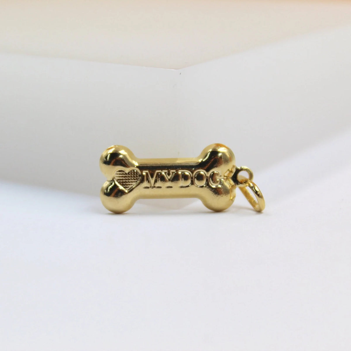 A polished gold bone pendant engraved with a heart and the text "MY DOG" rests on a white surface.