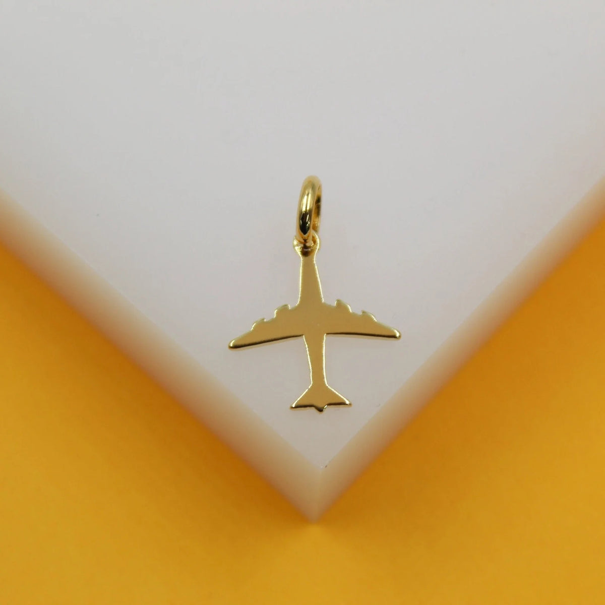 A shiny gold airplane pendant rests on a white display stand against a warm yellow background.