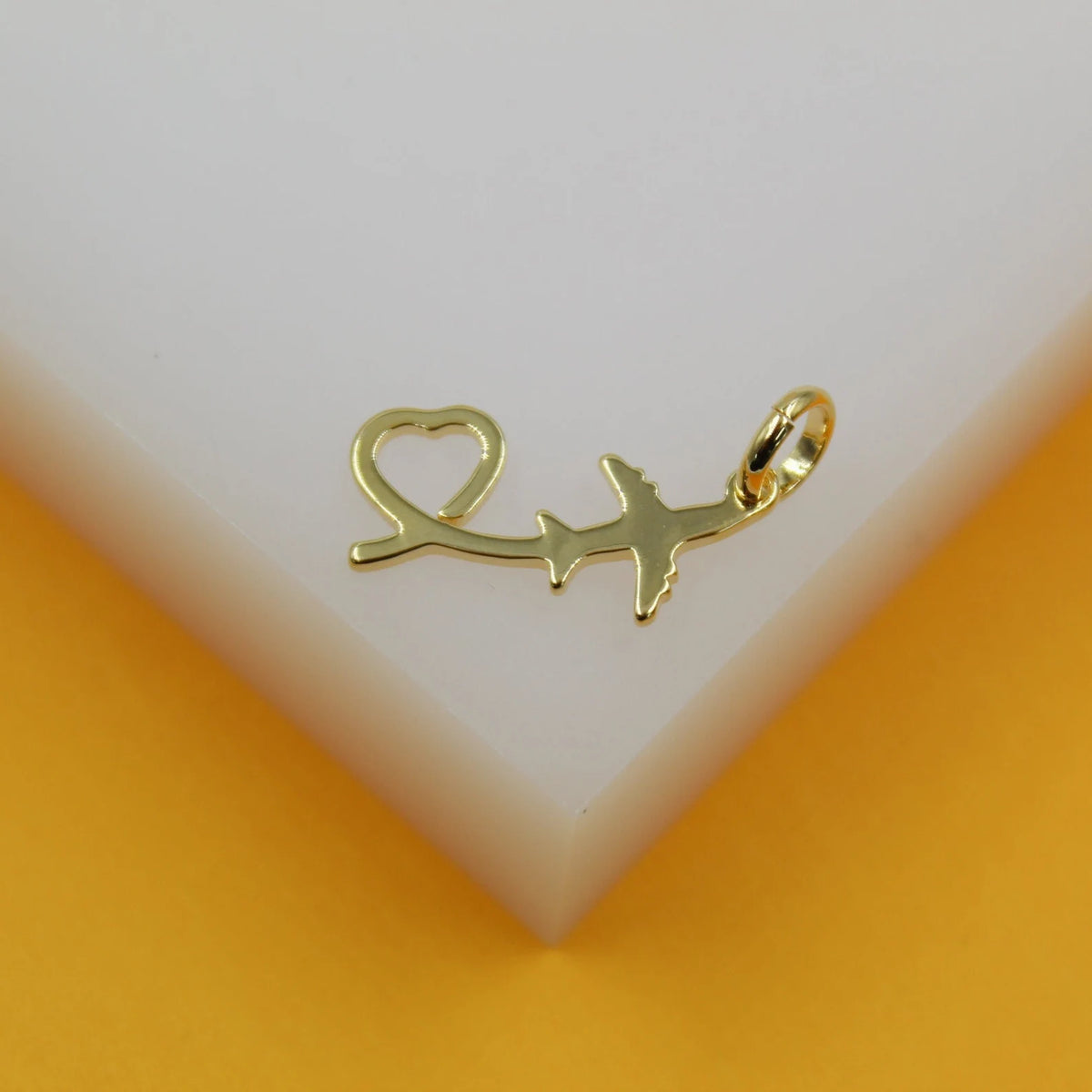 A gold airplane pendant with a heart-shaped trail rests on a white and yellow display surface.