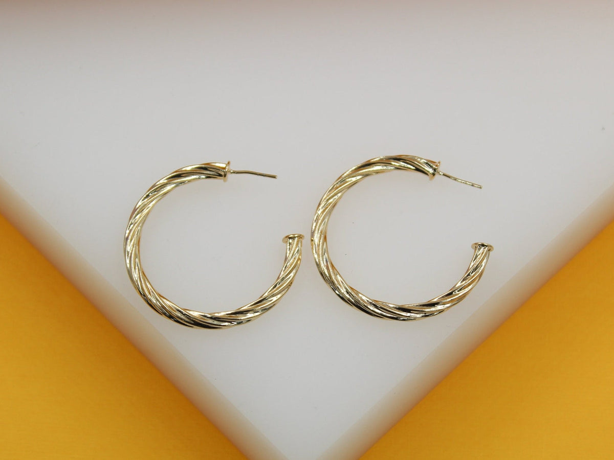 A pair of polished gold twist hoop earrings rests on a white and yellow display surface.