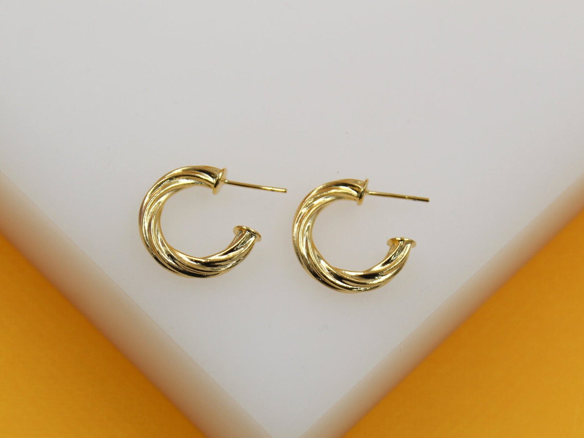 A pair of polished gold twist hoop earrings rests on a white display surface.