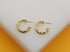 A pair of polished gold twist hoop earrings rests on a white display surface.