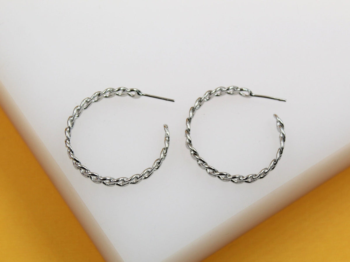 A pair of shiny silver twisted hoop earrings rests on a white display stand.
