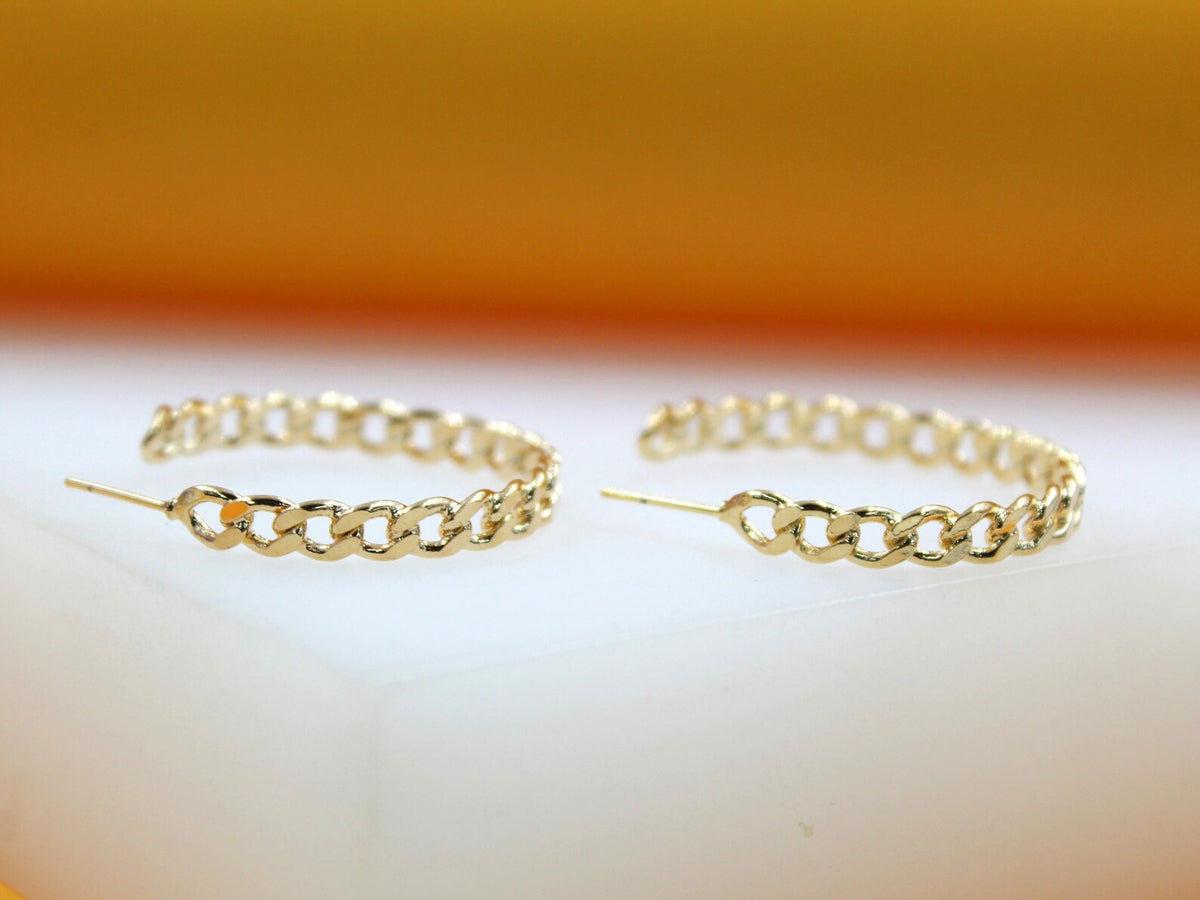 A pair of elegant gold chain-link hoop earrings rests on a white surface.
