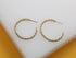 A pair of twisted gold chain hoop earrings rests neatly on a smooth white surface.