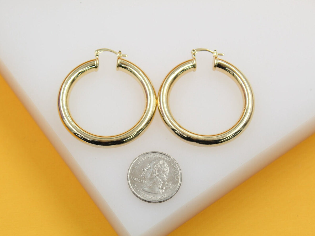 A pair of polished gold hoop earrings rests next to a US quarter on a white display surface.