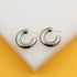 A pair of shiny silver chunky hoop earrings rests on a white display surface against a yellow background.