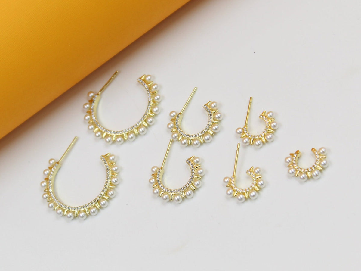 A graduated set of gold hoop earrings featuring sparkling pave crystals and delicate pearl accents is displayed on a neutral surface.