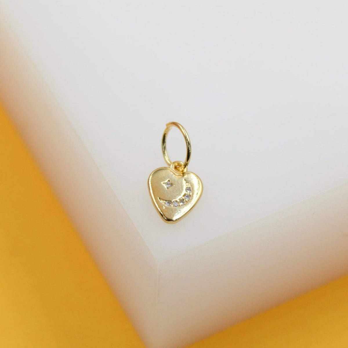 A gold heart-shaped charm hoop earring features a sparkling crescent moon and star design.