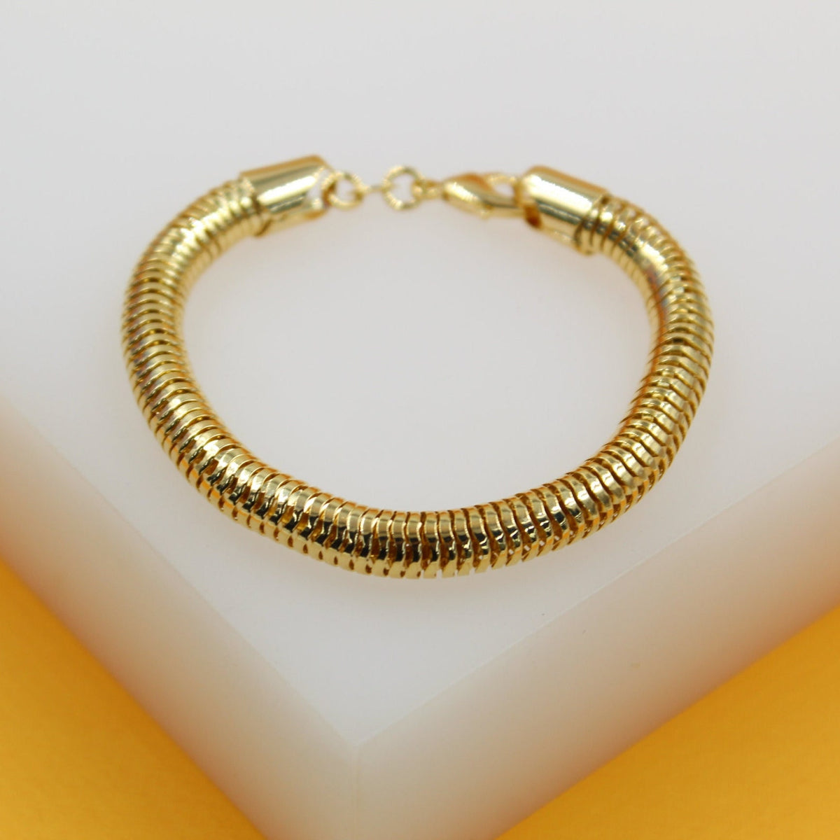 A gleaming gold snake chain bracelet rests on a white and yellow display block.
