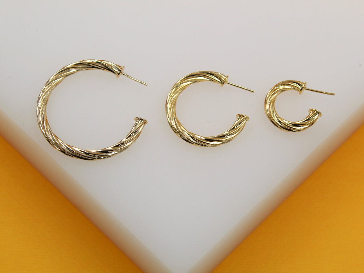 Three graduated sizes of twisted gold hoop earrings rest on a white surface against an orange backdrop.
