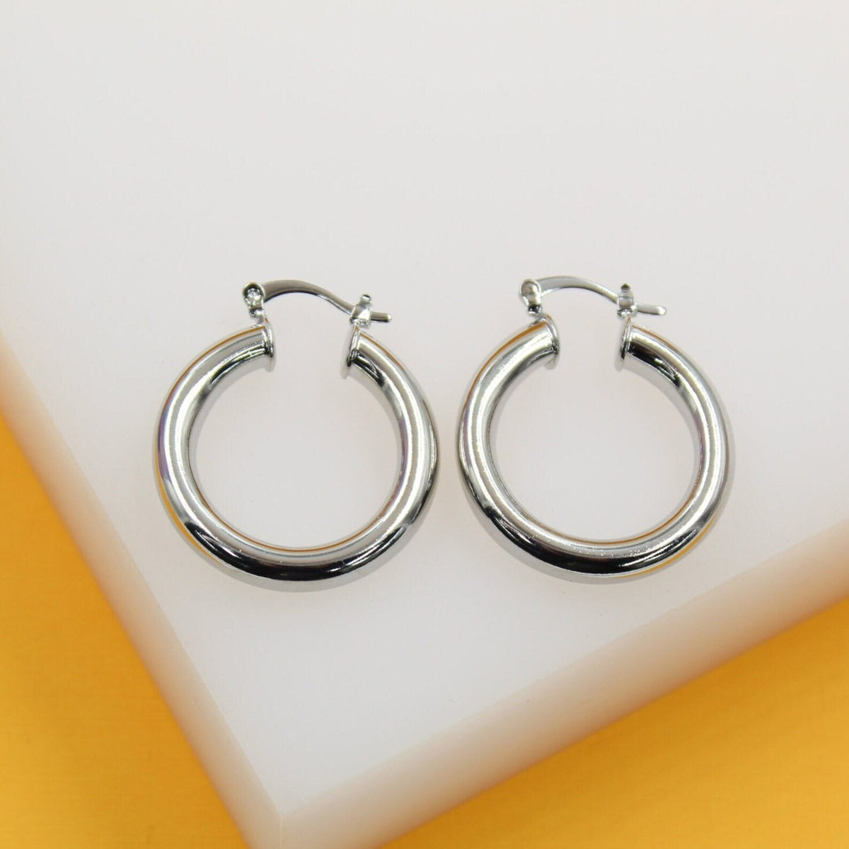 A pair of polished silver hoop earrings rests on a white display surface.