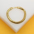 A shiny gold snake chain bracelet rests on a white display surface against a vibrant yellow background.
