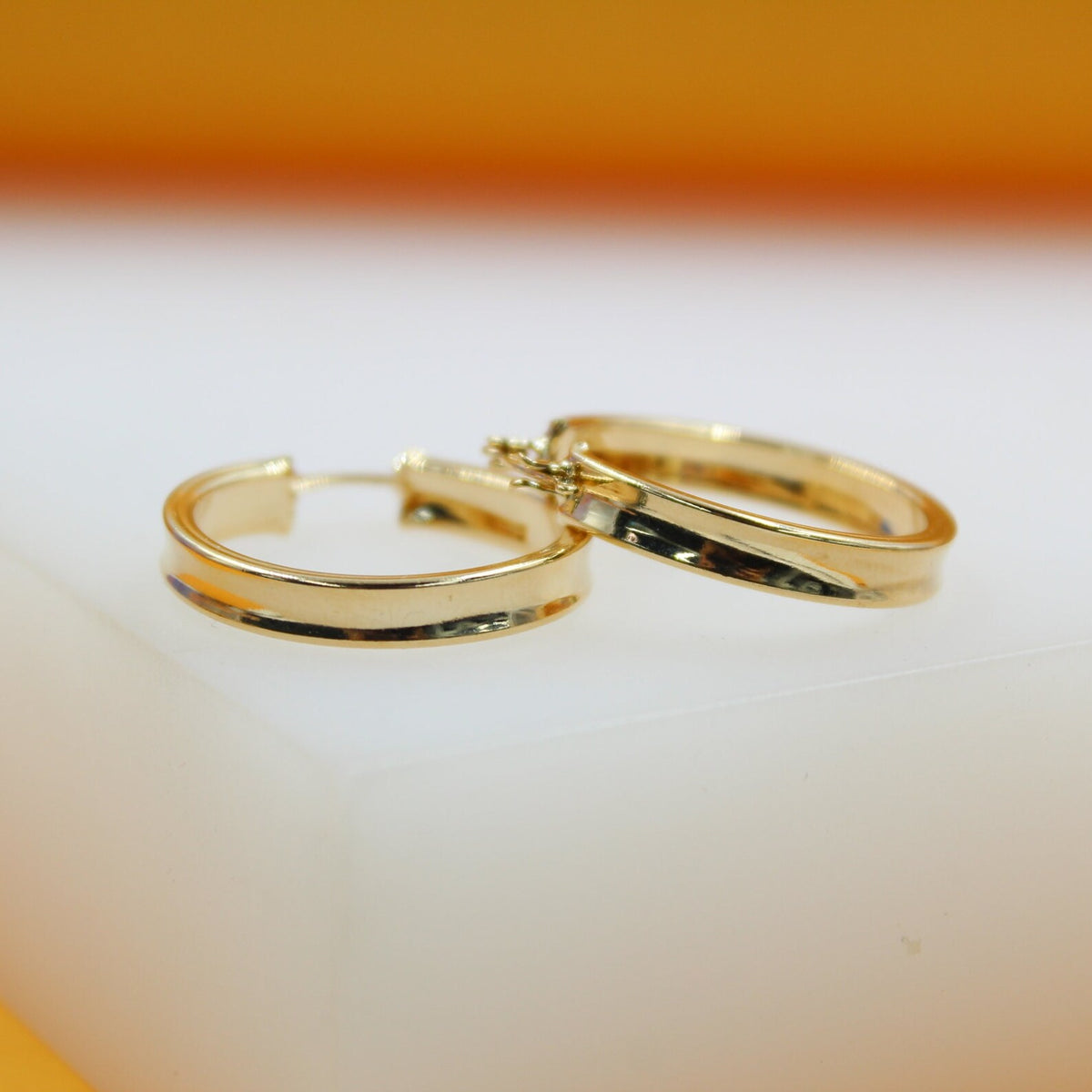 A pair of polished gold hoop earrings rests neatly on a white display surface.