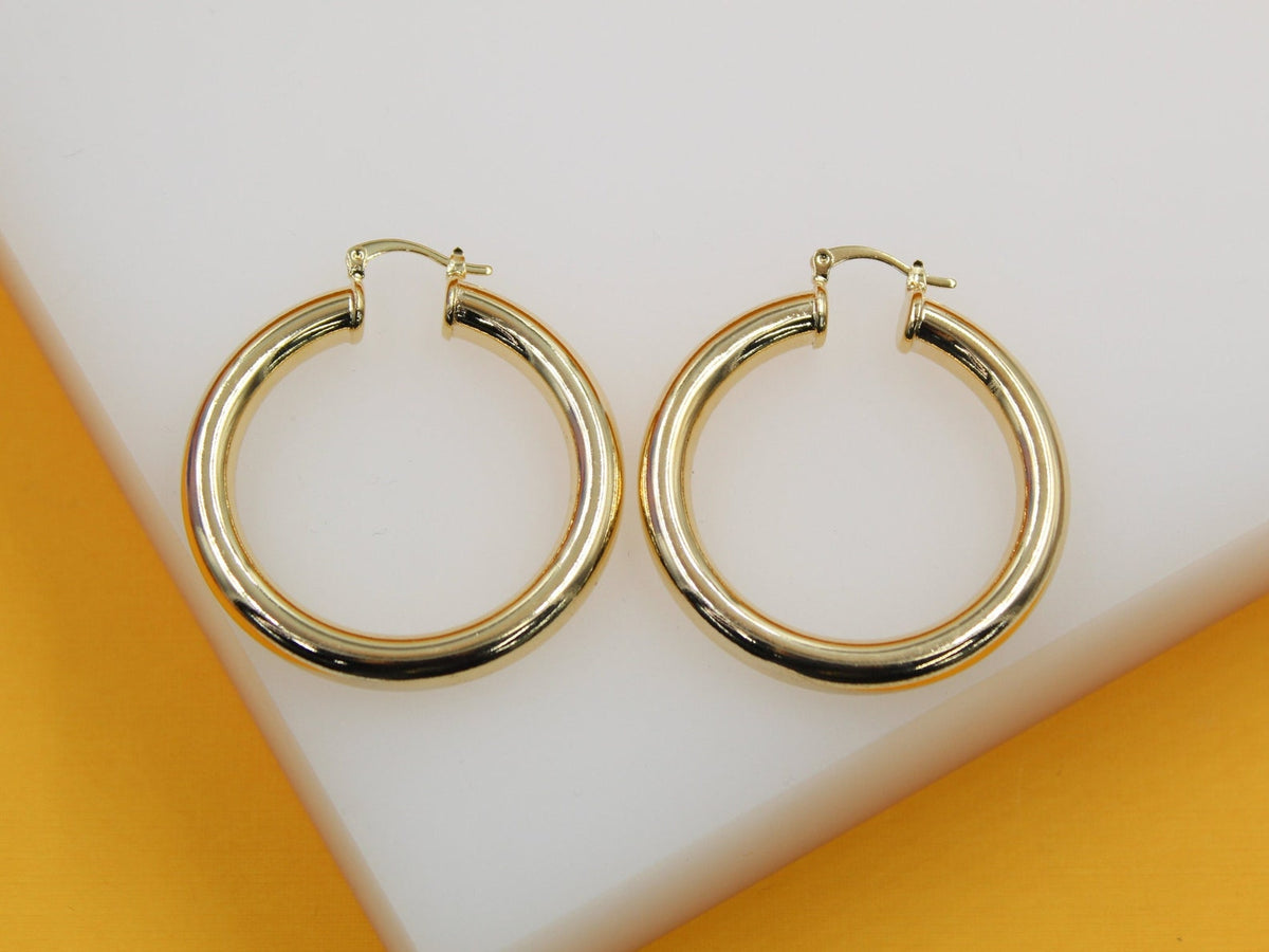A pair of thick gold hoop earrings rests neatly on a clean white surface against an orange backdrop.