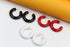 Three pairs of glossy, thick hoop earrings in black, red, and white rest on a white surface against an orange backdrop.