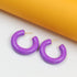 Glossy purple hoop earrings rest against a contrasting white and yellow background.