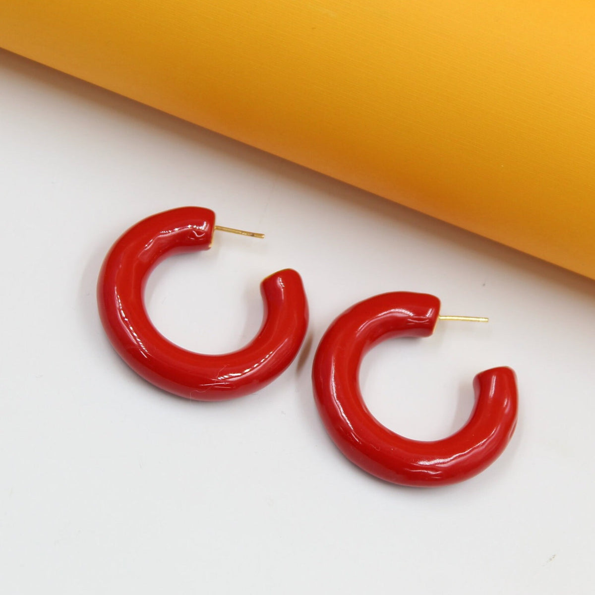 A pair of glossy red hoop earrings rests on a white and yellow background.