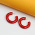 A pair of glossy red hoop earrings rests on a white and yellow background.