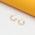 A pair of gold huggie hoop earrings decorated with delicate pearls and sparkling pave crystals rest against a white and yellow background.