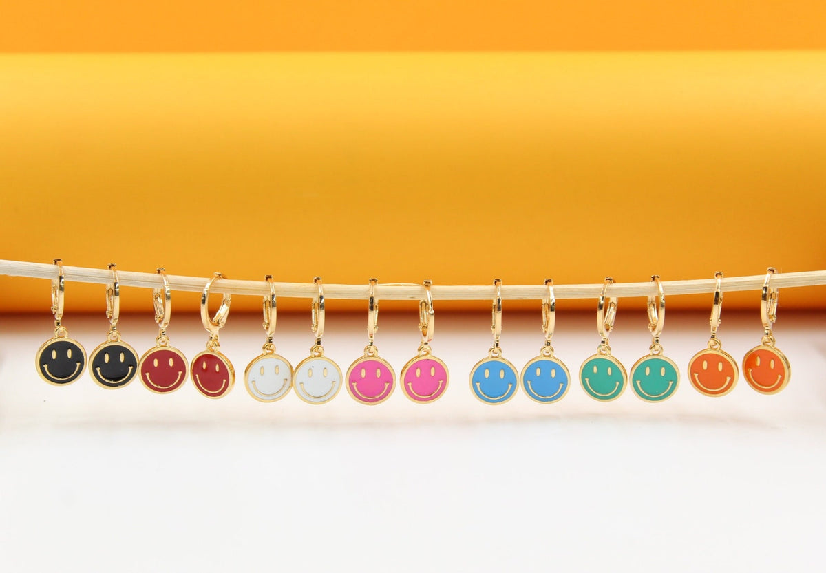 A horizontal line of colorful smiley face charm earrings hangs against a vibrant yellow and white background.