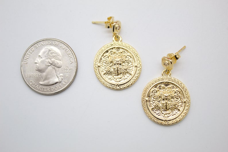 A pair of gold coin drop earrings sits next to a US quarter coin to show their size on a white background.