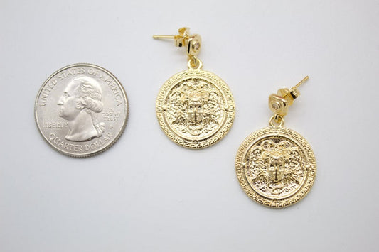 A pair of gold coin drop earrings sits next to a US quarter coin to show their size on a white background.