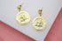 A pair of ornate gold Medusa coin dangle earrings rests on a white display surface.